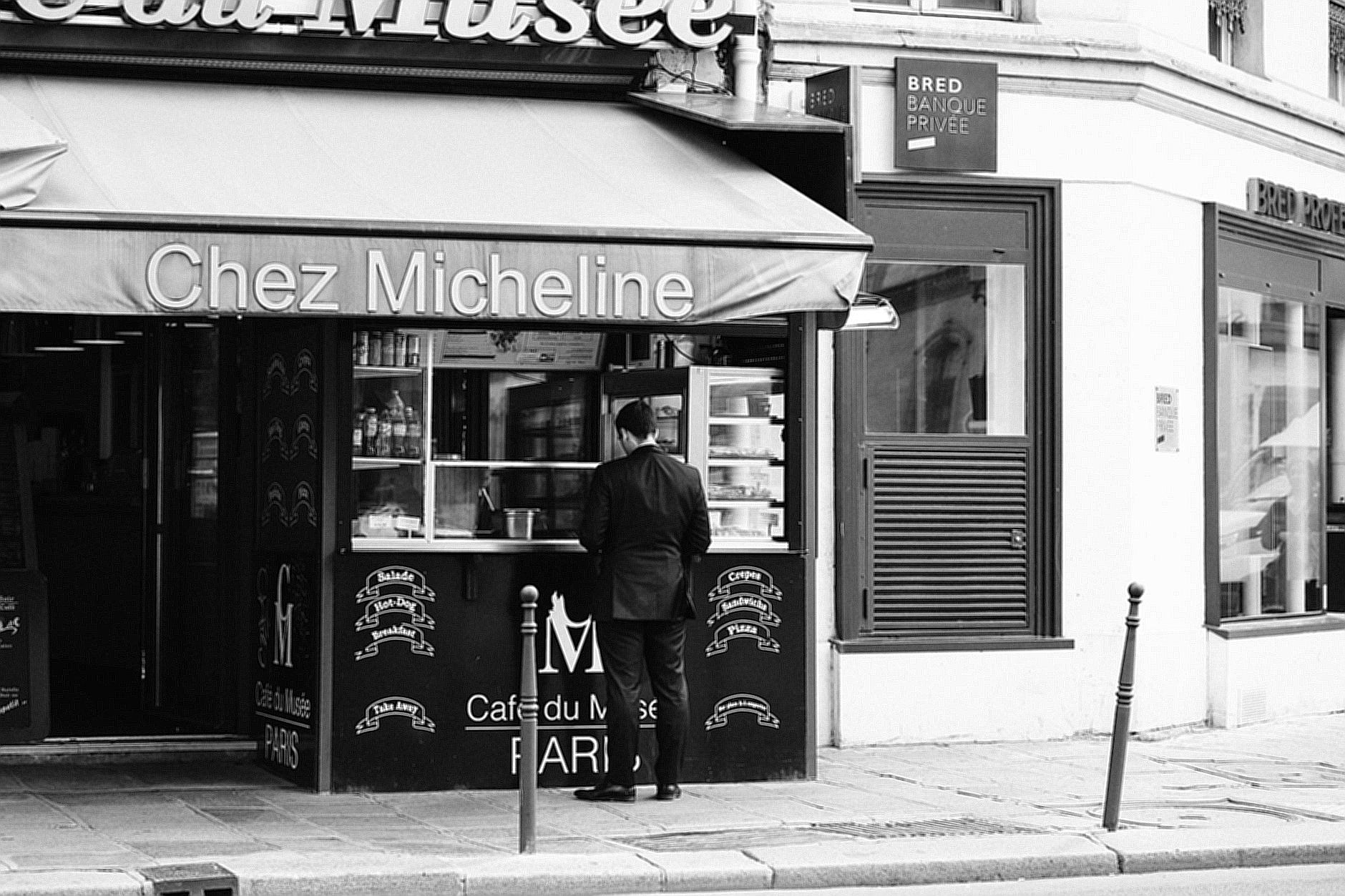 Grayscale Photo of Woman in Black Jacket Standing in Front of Store