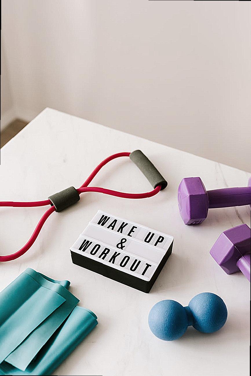 From above composition of dumbbells and massage double ball and tape and tubular expanders surrounding light box with wake up and workout words placed on white surface of table
