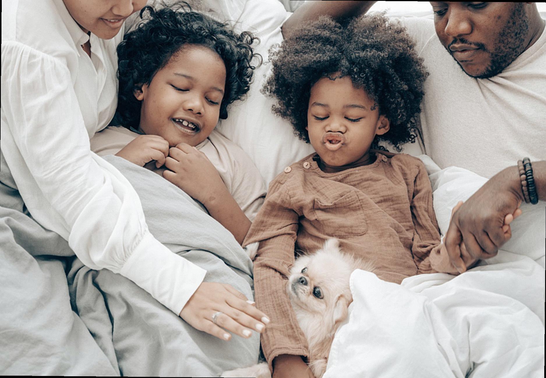 Happy ethnic family resting in bed with little dog