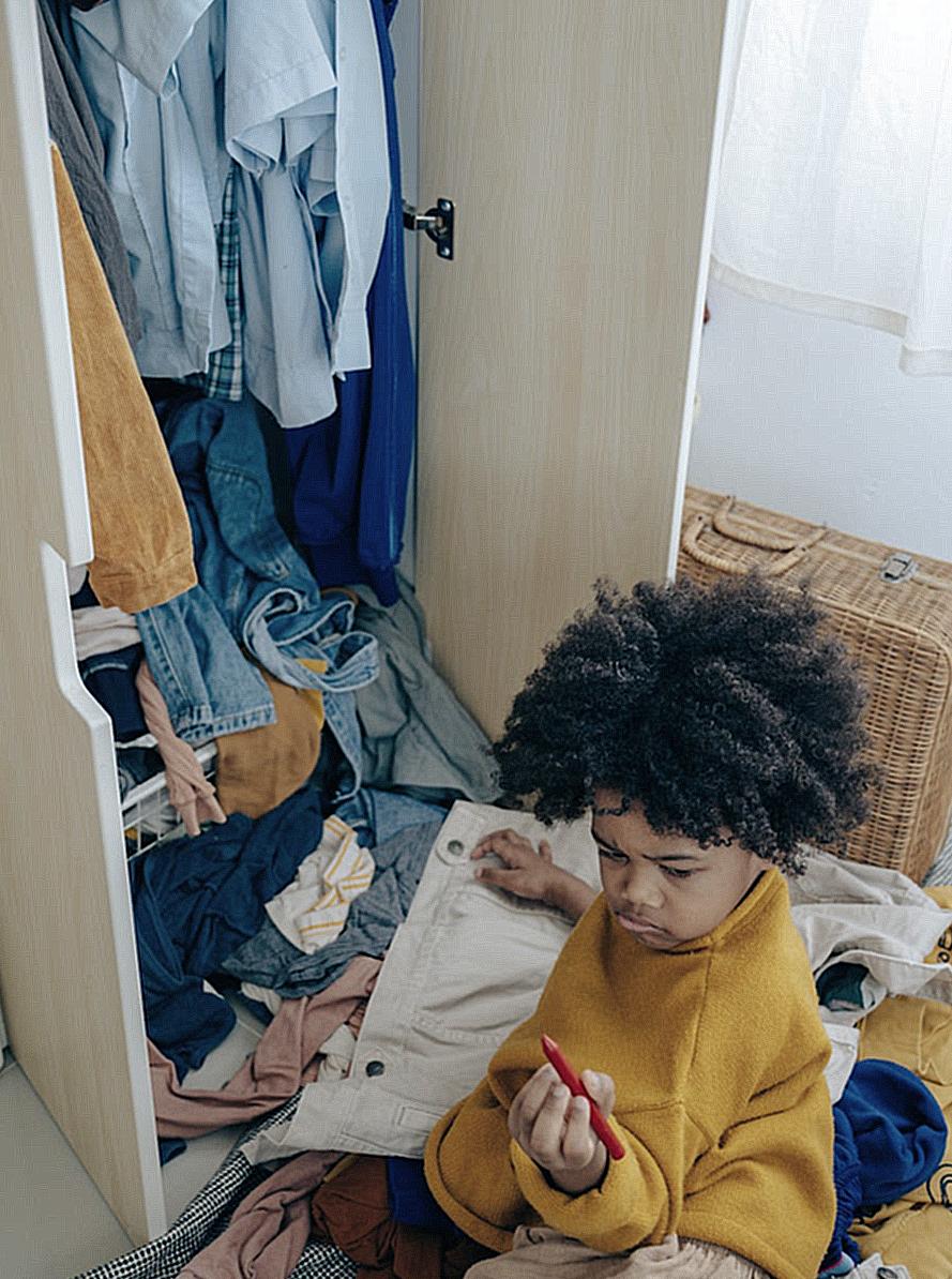 Curious little black kid making mess of clothes in wardrobe